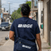 Pessoa uniformizada do IBGE caminha de costas em rua residencial durante trabalho de campo.