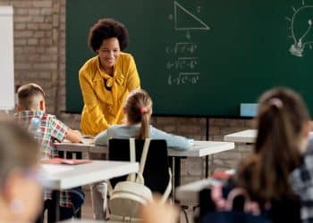 Professora de blusa amarela usando notebook em sala de aula durante inscrição na Prova Nacional Docente 2026