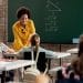 Professora de blusa amarela usando notebook em sala de aula durante inscrição na Prova Nacional Docente 2026