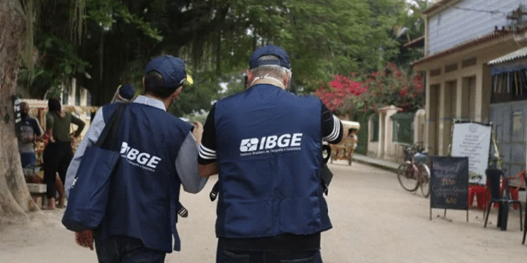 Dois agentes do IBGE de colete azul caminhando por uma rua durante trabalho de campo