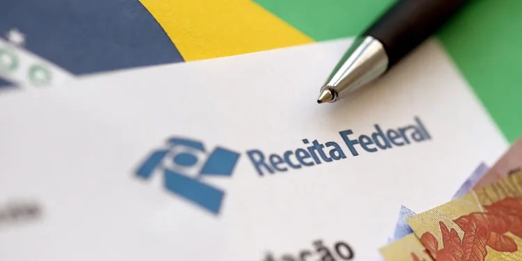 Documento da Receita Federal com caneta e cédulas representa a isenção do Imposto de Renda por doença grave.