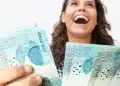 Mulher segurando cédulas de dinheiro representando liberação de pagamento de benefício de R$ 2.621 em julho