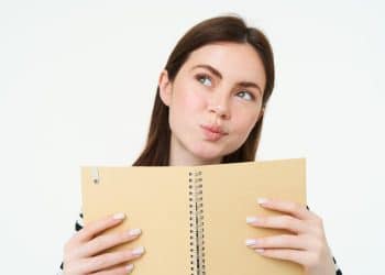 Mulher com expressão pensativa segurando um caderno aberto diante do rosto