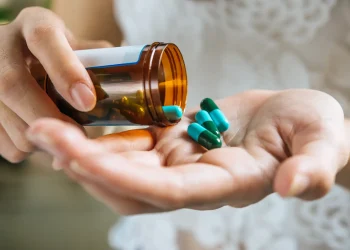 Pessoa segura frasco de medicamento e cápsulas, reforçando a importância da compra em estabelecimentos autorizados.