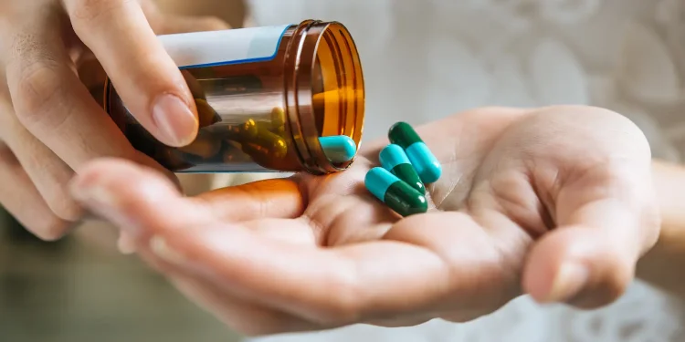 Pessoa segura frasco de medicamento e cápsulas, reforçando a importância da compra em estabelecimentos autorizados.