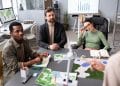 Equipe multidisciplinar analisa mapas e gráficos ao lado de maquetes de turbinas eólicas em reunião de projeto ambiental