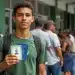 Jovem segura documentos pessoais durante mutirão da Carteira de Identidade Nacional com fila de atendimento em órgão público