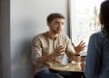 Homem gesticula enquanto fala com uma mulher em uma mesa de café, ilustrando o comportamento de quem fala em excesso