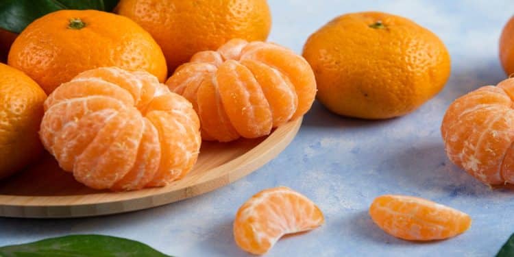 Tangerinas inteiras e descascadas sobre bandeja de madeira, fruta cujo nome gera dúvida entre as grafias ponkan e poncã.