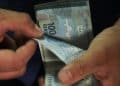 Mãos segurando e contando várias notas de 100 reais com detalhes nítidos, simbolizando o pagamento do BPC nos dias 6 e 7 de julho.