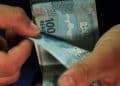 Pessoa conta cédulas de 100 reais, representando o pagamento do INSS liberado nesta sexta-feira, 3 de julho.