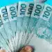 Notas de R$ 100 representando o pagamento, com valor de R$ 1.216 liberado em julho.