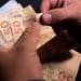 Pessoa contando várias cédulas de cinquenta reais sobre fundo escuro