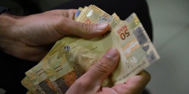 Mãos contam cédulas de 50 reais, referência ao Abono Salarial PIS/Pasep de até R$ 1.621 pago conforme o tempo trabalhado em 2024.
