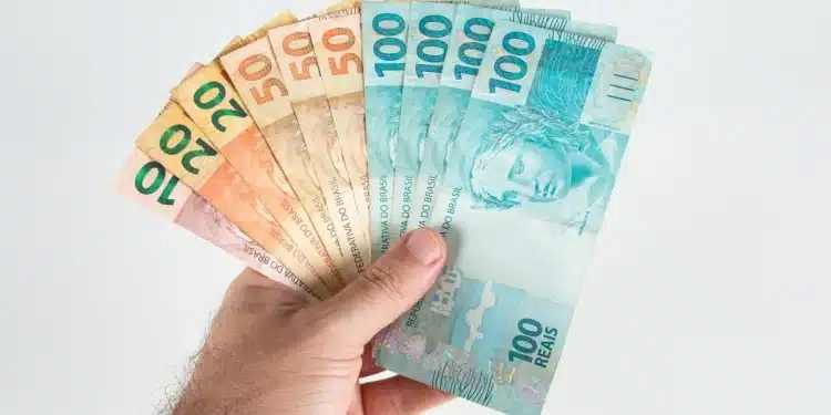 Mão segurando cédulas de real representando o pagamento de salários no quinto dia útil de julho
