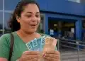 Mulher segurando cédulas de real em frente a uma entrada azul, representando pagamentos extras liberados em julho.