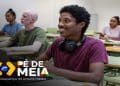 Estudante sorri em sala de aula com colegas ao fundo, ilustrando os alunos da EJA atendidos pelo Pé-de-Meia