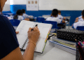 Professora fazendo anotações em agenda durante aula em sala de ensino fundamental, ilustrando investimentos do Fundeb na educação.