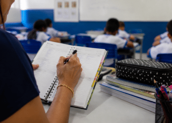 Professora fazendo anotações em agenda durante aula em sala de ensino fundamental, ilustrando investimentos do Fundeb na educação.