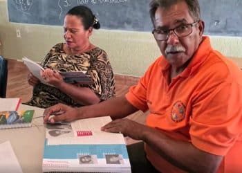 Dois estudantes adultos lendo livros didáticos durante aula em uma sala de Educação de Jovens e Adultos