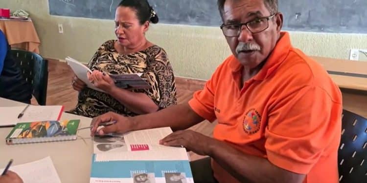 Dois estudantes adultos lendo livros didáticos durante aula em uma sala de Educação de Jovens e Adultos
