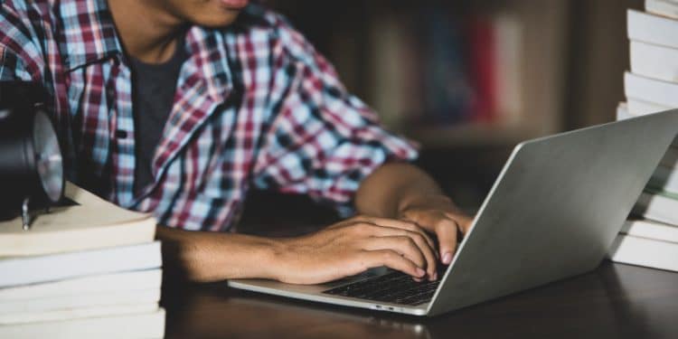 Imagem ilustrativa de estudante estudando com notebook e pilhas de livros, representando o Academia Enem 2026, cursinho gratuito da Prefeitura de Fortaleza com 8 mil vagas para o exame.