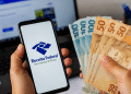 Celular com acesso à Receita Federal ao lado de notas de dinheiro representando dados de renda média dos trabalhadores brasileiros.