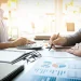 Profissionais analisam gráficos e dados financeiros em uma mesa de trabalho com calculadora e documentos.
