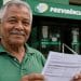 Aposentado sorridente segura documento em frente a uma agência da Previdência Social, referência à proposta de recálculo do benefício do INSS