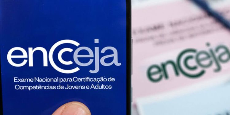 Celular exibindo o logotipo do Encceja, com folhas de prova desfocadas ao fundo