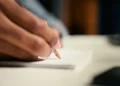 Estudante escreve redação do Enem em folha de papel durante preparação para alcançar nota 1000 na prova.