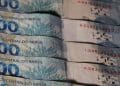 Notas de 100 reais enfileiradas, ilustrando os valores do abono salarial, do lote extra e do ressarcimento das cotas do PIS/PASEP.