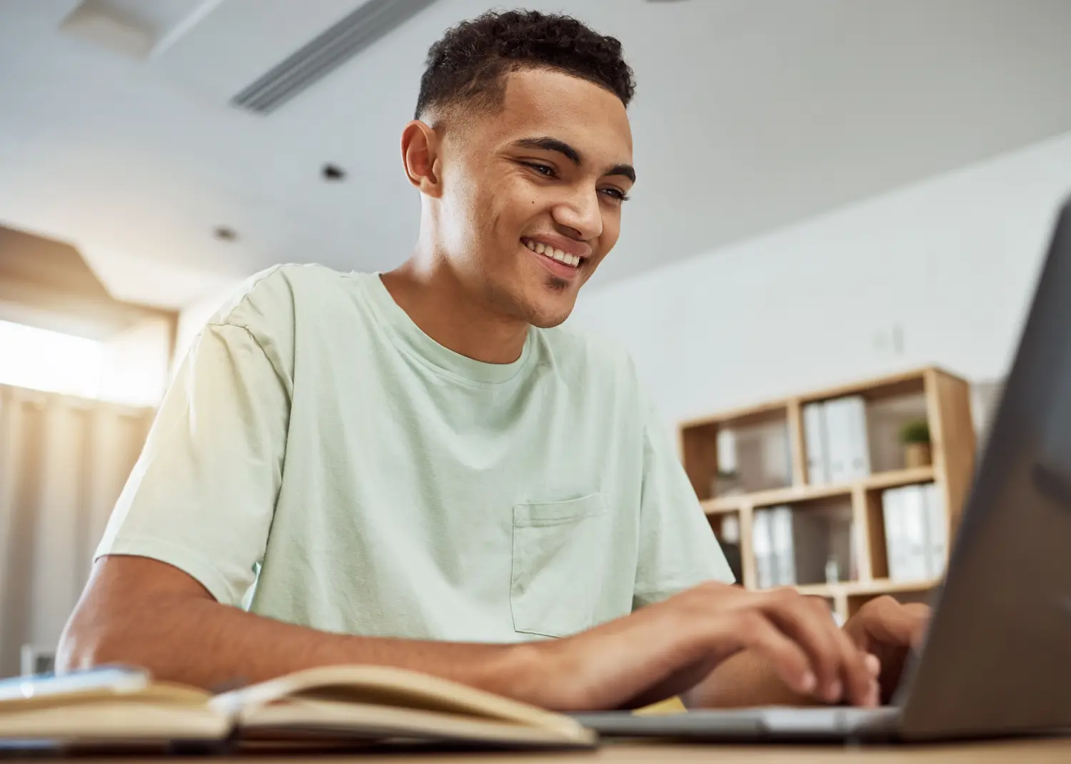 Estudante sorri enquanto usa o notebook em uma mesa de estudos, imagem que representa a consulta do candidato pré-selecionado no Prouni 2026/2