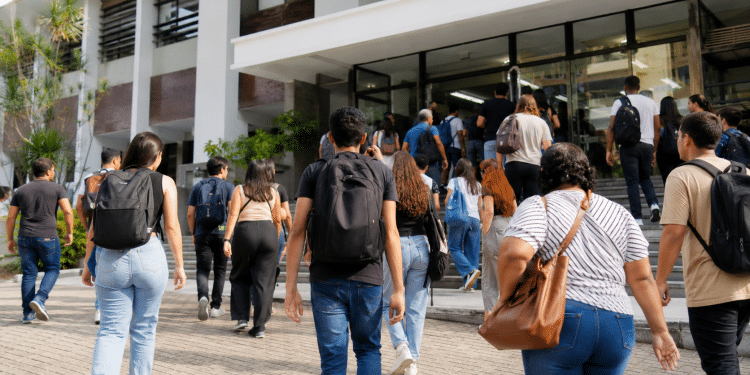 Grupo de jovens e adultos caminhando com mochilas em direção a uma faculdade, representando estudantes interessados no Prouni.