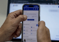 Mãos segurando celular aberto no app Meu INSS com tela de serviços e botão “Consultar Benefício”, simbolizando os serviços do Meu INSS.