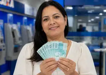 Mulher segura notas de R$ 100 em uma agência bancária, representando o saque de R$ 6.220 do FGTS.