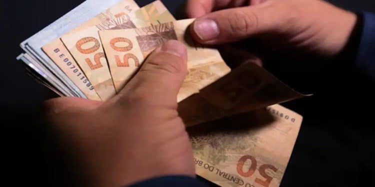 Mãos contam cédulas de cinquenta reais, representando o dinheiro esquecido que pode ser resgatado pelo Sistema de Valores a Receber