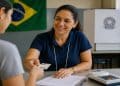 Imagem ilustrativa de mesária entregando o comprovante de votação à eleitora, tarefa de quem trabalha na urna e tem direito a folgas e auxílio-alimentação nas Eleições 2026